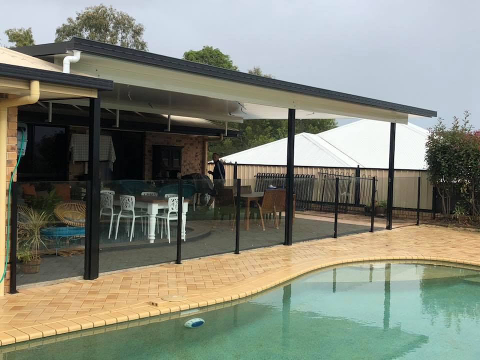 Semi-frameless glass pool fence with black posts beside a poolside alfresco